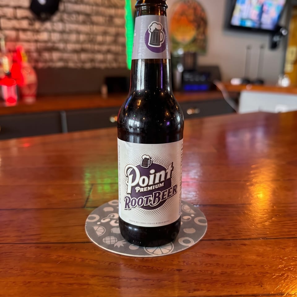 Point Premium Root Beer bottle on a coaster at a warmly lit restaurant bar with neon signs and televisions.